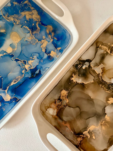 Close-up of hand painted ceramic handle trays in blue and neutral tones with gold accents